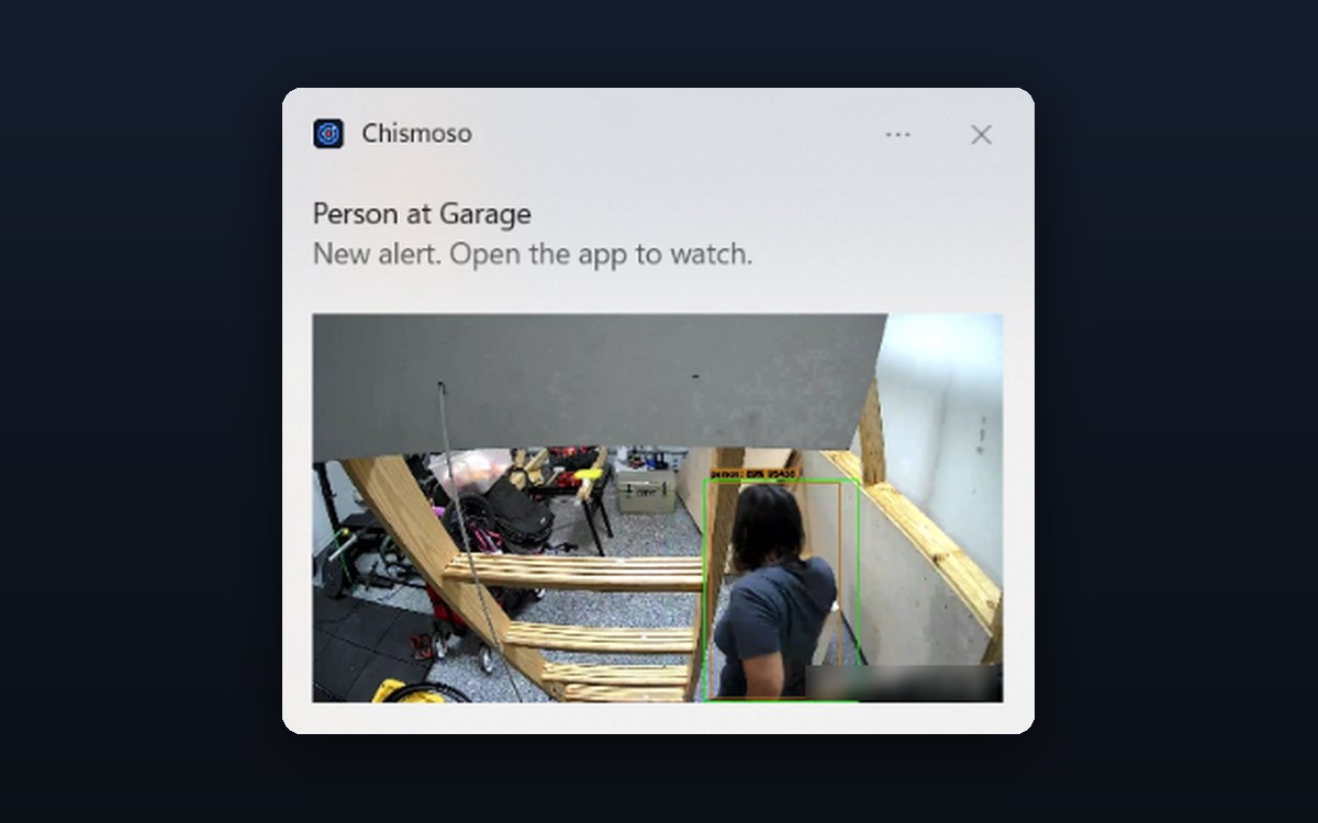 A Windows notification from Chismoso: “Person at Garage. New alert. Open the app to watch.” with a camera snapshot of the person outlined.